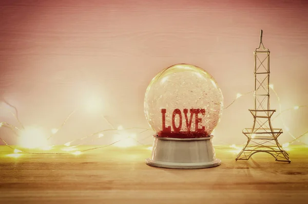 Valentine's day background. Water globe with word LOVE and glitter over the wooden table and pink bakground