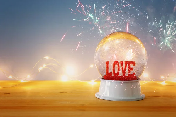 Valentine's day background. Water globe with word LOVE and glitter over the wooden table and blue bakground. Fireworks overlay