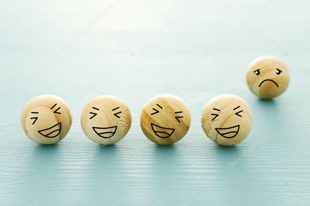 concept of bullying , discrimination. group of laughing emoticon faces and one alone look sad and depressed