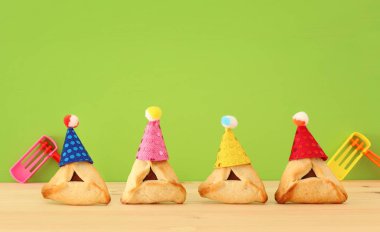 Purim kutlama kavramı (Yahudi karnaval tatil). Sevimli palyaço şapkalar ve şenlikli ahşap masa üzerinde ile geleneksel hamantaschen tatlılar