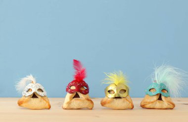 Purim kutlama kavramı (Yahudi karnaval tatil). Ahşap masa ve mavi arka plan üzerinde şirin maskeleri ile geleneksel hamantaschen tanımlama