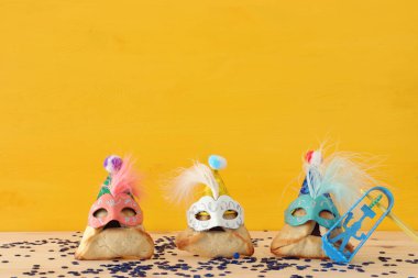 Purim kutlama kavramı (Yahudi karnaval tatil). Sevimli palyaço şapkalar ve ahşap masa üzerinde maskeleri ile geleneksel hamantaschen tatlılar