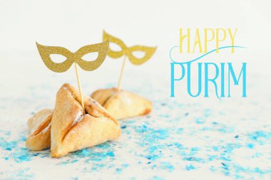 Purim kutlama kavramı (Yahudi karnaval tatil). Beyaz ahşap masa üzerinde şirin altın maske ile geleneksel hamantaschen tanımlama