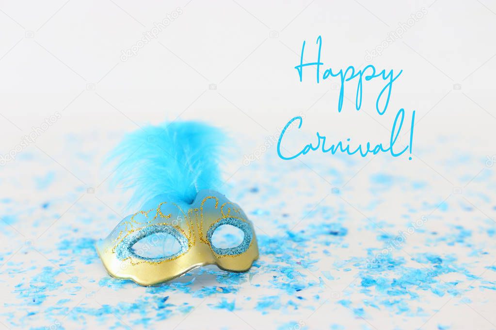 carnival party celebration concept with elegant gold and blue mask over white wooden background with confetti