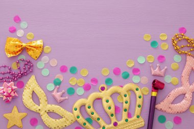 Karnaval parti kutlama kavramı maskesi ve mor ahşap arka plan üzerinde renkli parti aksesuarları ile. Üstten görünüm. Düz yatıyordu