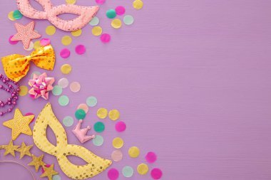 Karnaval parti kutlama kavramı maskesi ve mor ahşap arka plan üzerinde renkli parti aksesuarları ile. Üstten görünüm. Düz yatıyordu