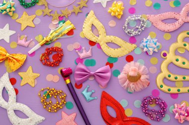 Karnaval parti kutlama kavramı maskesi ve mor ahşap arka plan üzerinde renkli parti aksesuarları ile. Üstten görünüm. Düz yatıyordu