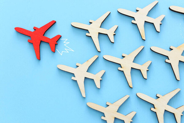 Leadership concept with airplanes on blue wooden background. One red leader flays ahead others.