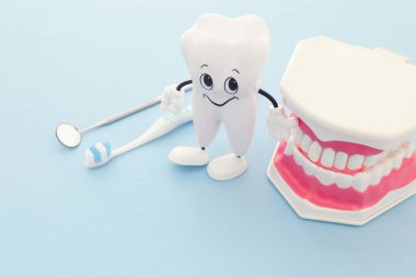 Diş hekimi, mutlu sağlıklı dişler ve klinik modelde plastik diş diş bakımı araçlarını kullanın. Ahşap mavi arka plan