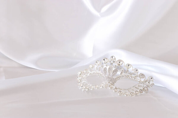 Photo of elegant and delicate silver diamond venetian mask over white silk background