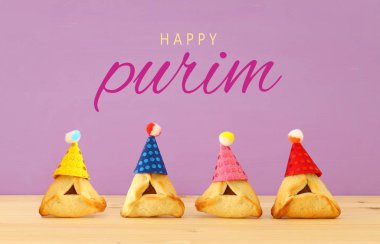 Purim kutlama kavramı (Yahudi karnaval tatil). Sevimli palyaço şapka ahşap masa ve mor arka plan ile geleneksel hamantaschen tanımlama