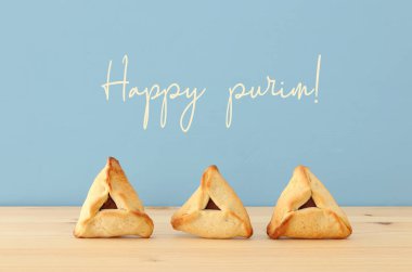 Purim kutlama kavramı (Yahudi karnaval tatil). Geleneksel hamantaschen çerezler ahşap masa ve mavi arka plan üzerinde