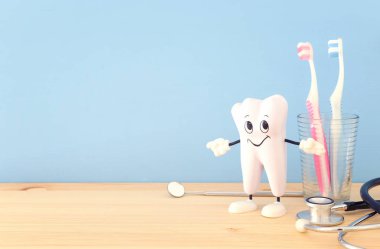 Diş hekimi ve sağlıklı diş kliniğinde gülümseyen için diş bakımı araçlarını kullanın. Ahşap mavi arka plan