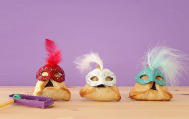 Purim kutlama kavramı (Yahudi karnaval tatil). Sevimli palyaço şapkalar ve ahşap masa üzerinde maskeleri ile geleneksel hamantaschen tatlılar