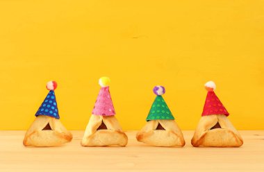 Purim kutlama kavramı (Yahudi karnaval tatil). Sevimli palyaço şapka ahşap masa ve sarı arka plan ile geleneksel hamantaschen tanımlama