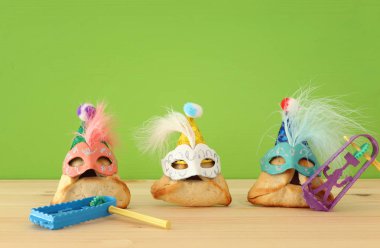 Purim kutlama kavramı (Yahudi karnaval tatil). Sevimli palyaço şapkalar ve ahşap masa üzerinde maskeleri ile geleneksel hamantaschen tatlılar