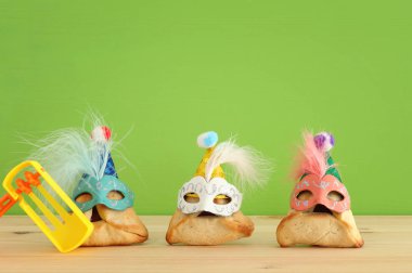 Purim kutlama kavramı (Yahudi karnaval tatil). Sevimli palyaço şapkalar ve ahşap masa üzerinde maskeleri ile geleneksel hamantaschen tatlılar
