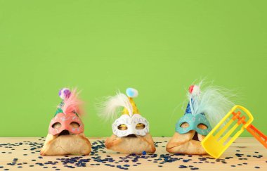 Purim kutlama kavramı (Yahudi karnaval tatil). Sevimli palyaço şapkalar ve ahşap masa üzerinde maskeleri ile geleneksel hamantaschen tatlılar