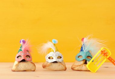 Purim kutlama kavramı (Yahudi karnaval tatil). Sevimli palyaço şapkalar ve ahşap masa üzerinde maskeleri ile geleneksel hamantaschen tatlılar