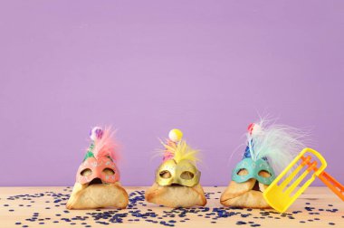 Purim kutlama kavramı (Yahudi karnaval tatil). Sevimli palyaço şapkalar ve ahşap masa üzerinde maskeleri ile geleneksel hamantaschen tatlılar
