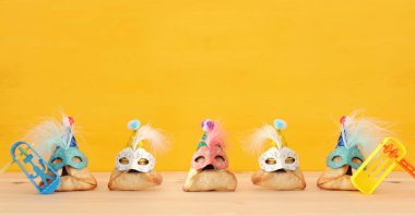 Purim kutlama kavramı (Yahudi karnaval tatil). Sevimli palyaço şapkalar ve ahşap masa üzerinde maskeleri ile geleneksel hamantaschen tatlılar