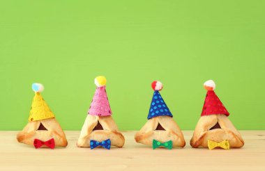 Purim kutlama kavramı (Yahudi karnaval tatil). Sevimli palyaço şapka ahşap masa ve yeşil arka plan ile geleneksel hamantaschen tanımlama