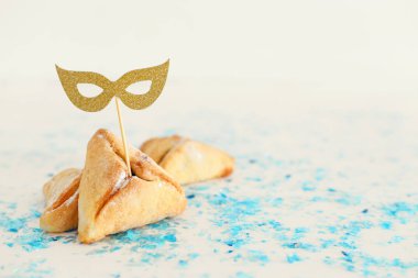Purim kutlama kavramı (Yahudi karnaval tatil). Maskeyi Beyaz ahşap masa üzerine ile geleneksel hamantaschen tanımlama