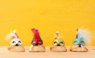 Purim kutlama kavramı (Yahudi karnaval tatil). Ahşap masa ve sarı arka plan üzerinde şirin maskeleri ile geleneksel hamantaschen tanımlama.