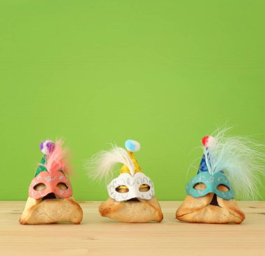 Purim kutlama kavramı (Yahudi karnaval tatil). Ahşap masa ve yeşil renkli sevimli maskeleri ile geleneksel hamantaschen tanımlama.