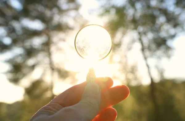 Una mano maschile tiene una lente d'ingrandimento contro il sole che tramonta all'esterno. concetto di ricerca, pensiero creativo e uso dell'energia solare — Foto Stock
