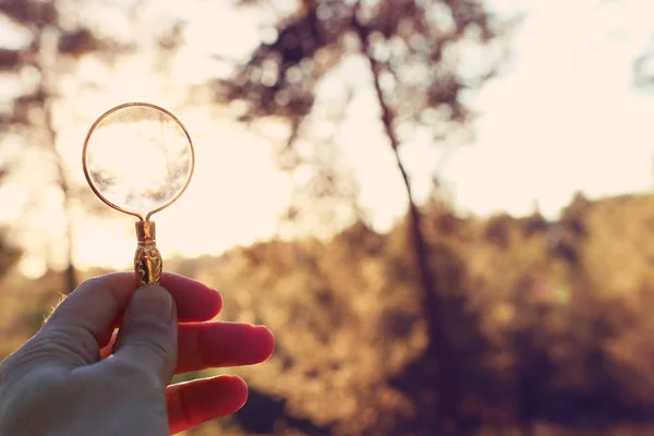 Een mannenhand bezit een vergrootglas tegen de ondergaande zon buiten. concept van zoeken, creatief denken en het gebruik van zonne-energie — Stockfoto