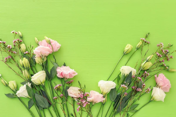 Frühlingsstrauß aus Pastell und zartrosa Blumen auf grünem Holzgrund. Draufsicht, flache Lage — Stockfoto