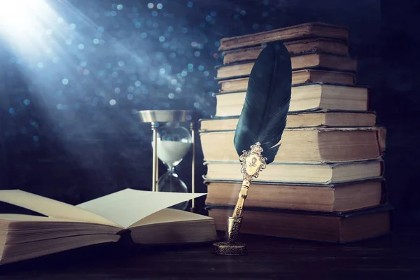 Old feather quill ink pen with inkwell and old books over wooden desk in front of black wall background. Conceptual photo on history, fantasy, education and literature topic — Stock Photo, Image