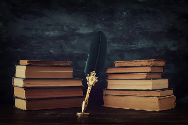 Παλιά πένα φτερό μελάνι στυλό με μελανοδοχείο και παλιά βιβλία πάνω από το ξύλινο γραφείο μπροστά από μαύρο φόντο τοίχο. Εννοιολογική φωτογραφία με θέμα την ιστορία, τη φαντασία, την εκπαίδευση και τη λογοτεχνία — Φωτογραφία Αρχείου