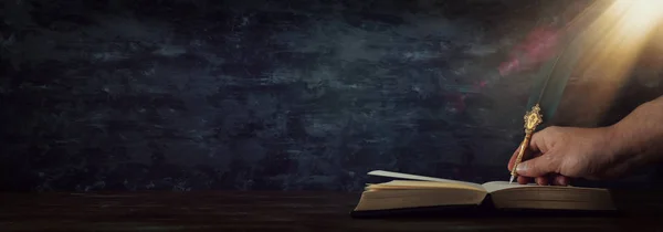 Old feather quill ink pen with inkwell and old books over wooden desk in front of black wall background. Conceptual photo on history, fantasy, education and literature topic — Stock Photo, Image