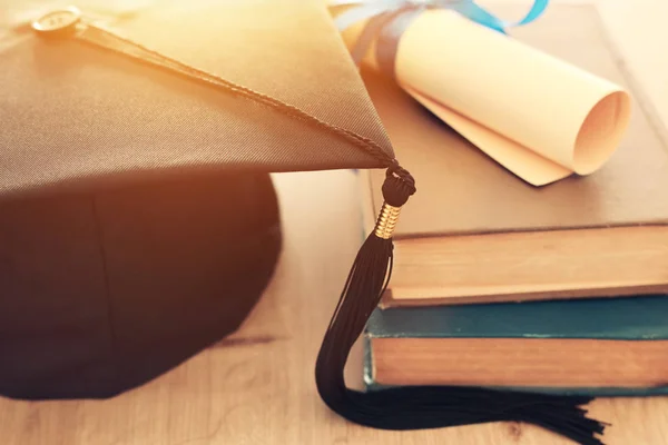 Foto de la graduación sombrero negro sobre libros antiguos junto al diploma de desplazamiento en el escritorio de madera. Educación y vuelta al concepto escolar —  Fotos de Stock