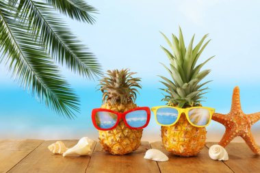 Mavi denize karşı ahşap masa veya güverte üzerinde şık güneş gözlüğü olgun çift ananas, rahatlatıcı. Tropikal yaz tatili konsepti.