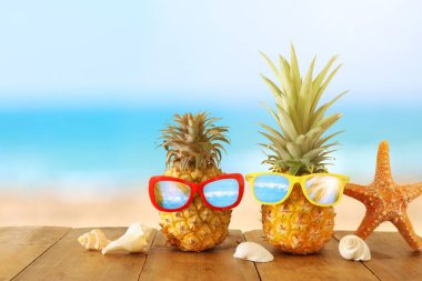 Mavi denize karşı ahşap masa veya güverte üzerinde şık güneş gözlüğü olgun çift ananas, rahatlatıcı. Tropikal yaz tatili konsepti.