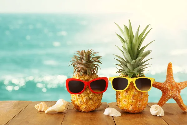 Mogen par ananas i snygga solglasögon över träbord eller däck mot blått hav, avslappnande. Tropiskt sommarlov koncept. — Stockfoto