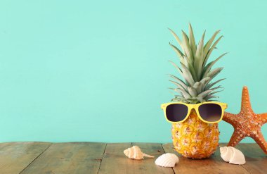 Ahşap masa veya güverte rahatlatıcı üzerinde şık güneş gözlüğü olgun ananas. Tropikal yaz tatili konsepti