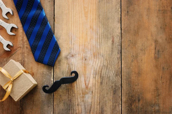 Concepto del día del padre. Caja de regalo, corbata y divertido bigote sobre fondo de madera. vista superior, plano — Foto de Stock