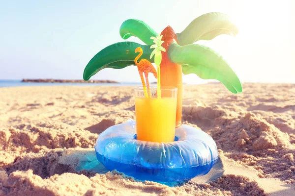 Concepto de vacaciones y verano con bebida de fruta fresca y piscina en forma de palma flotan sobre la arena en la playa — Foto de Stock