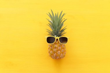 Ahşap sarı arka plan üzerinde şık güneş gözlüğü olgun ananas. Tropikal yaz tatili konsepti. üst vew