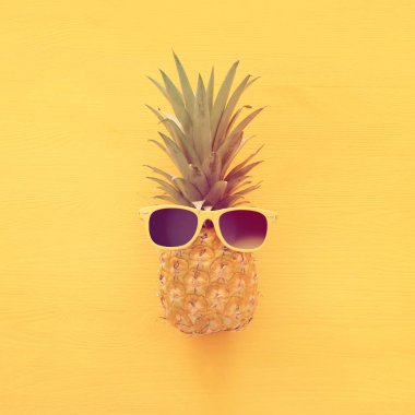Ahşap sarı arka plan üzerinde şık güneş gözlüğü olgun ananas. Tropikal yaz tatili konsepti. üst vew