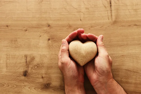 Adult male hands holding wooden shaped heart over table — Stock Photo, Image