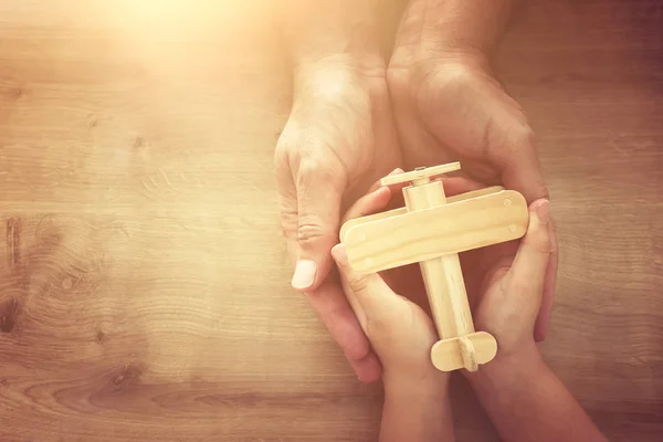 Foto von Vater und Kind, die ein Spielzeugflugzeug aus Holz zusammenhalten. Vatertags- und Urlaubskonzept. Draufsicht, oben — Stockfoto