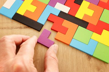 Bir adamın eli ahşap bir masanın üzerinde kare bir tangram yapbozu tutuyor.