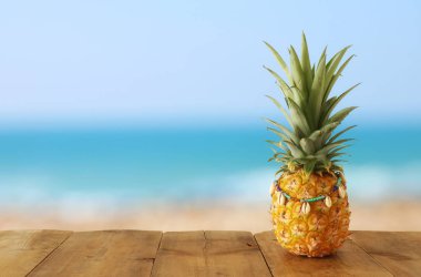 Plaj ve tropikal arka plan önünde ahşap masa üzerinde Olgun ananas