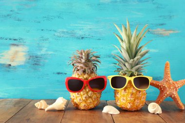Ahşap masa veya güverte üzerinde şık güneş gözlüğü olgun çift ananas, rahatlatıcı. Tropikal yaz tatili konsepti