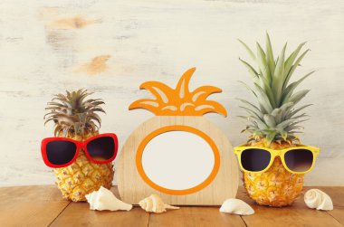 Boş fotoğraf çerçevesi ve güneş gözlüğü ile komik ananas çift. Fotoğraf ve not defteri montajı için